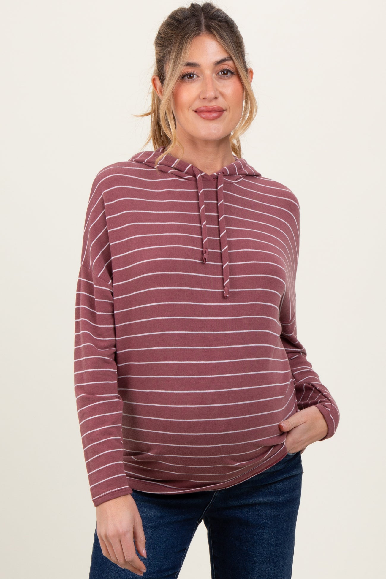 woman wearing a maroon striped maternity hoodie with a baby bump visible and blue jeans