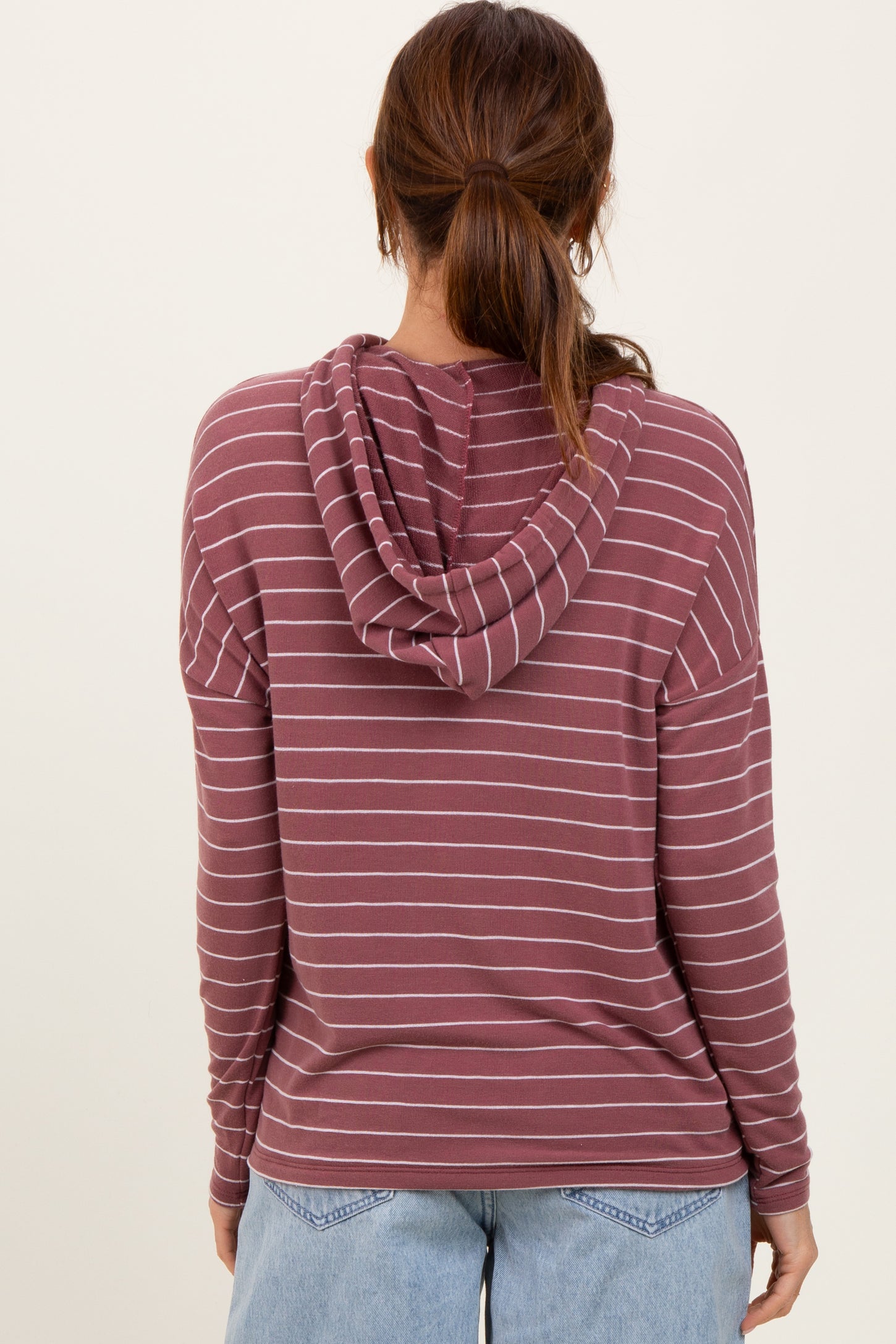 woman wearing a burgundy and white striped long sleeve hoodie with a drawstring hood, viewed from the back