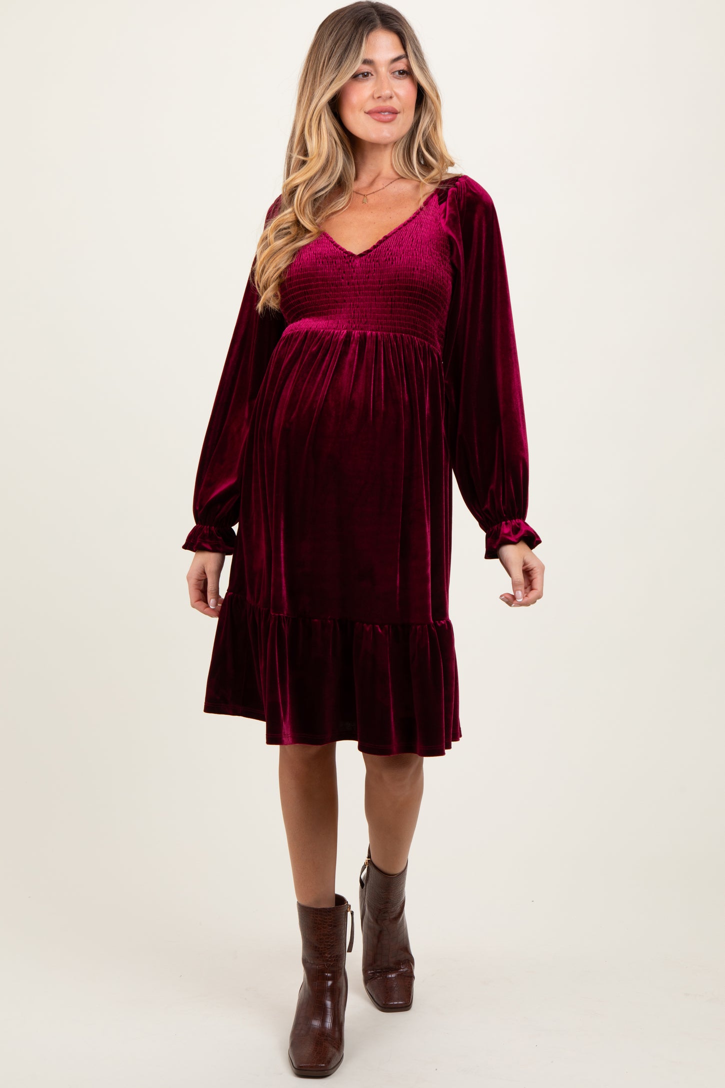 woman wearing a burgundy velvet maternity dress with a smocked bodice and long sleeves, showing her baby bump