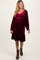 woman wearing a burgundy velvet maternity dress with a smocked bodice and long sleeves, showing her baby bump