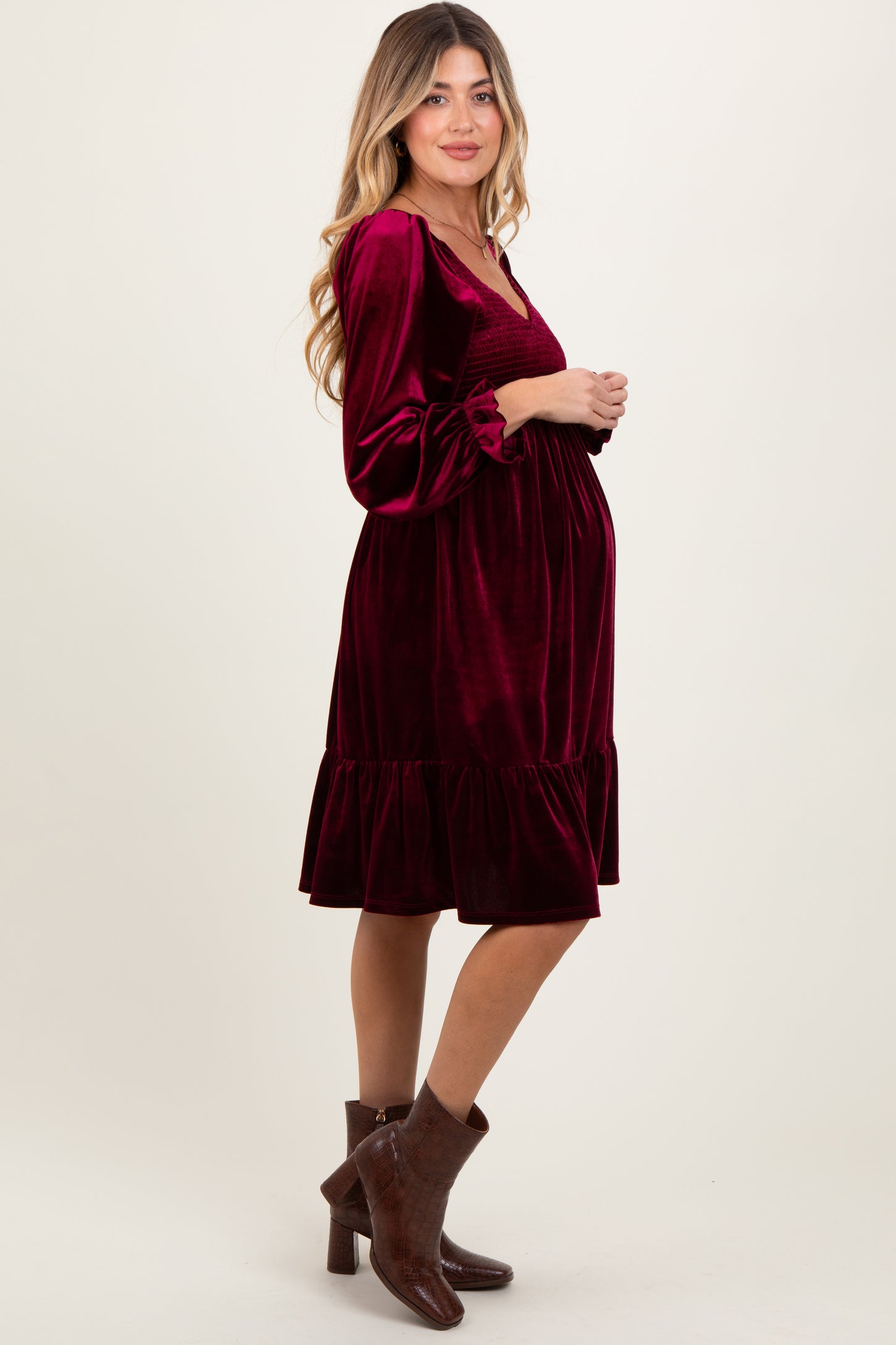 woman wearing a burgundy velvet maternity dress with long sleeves and a ruffled hem, highlighting her baby bump