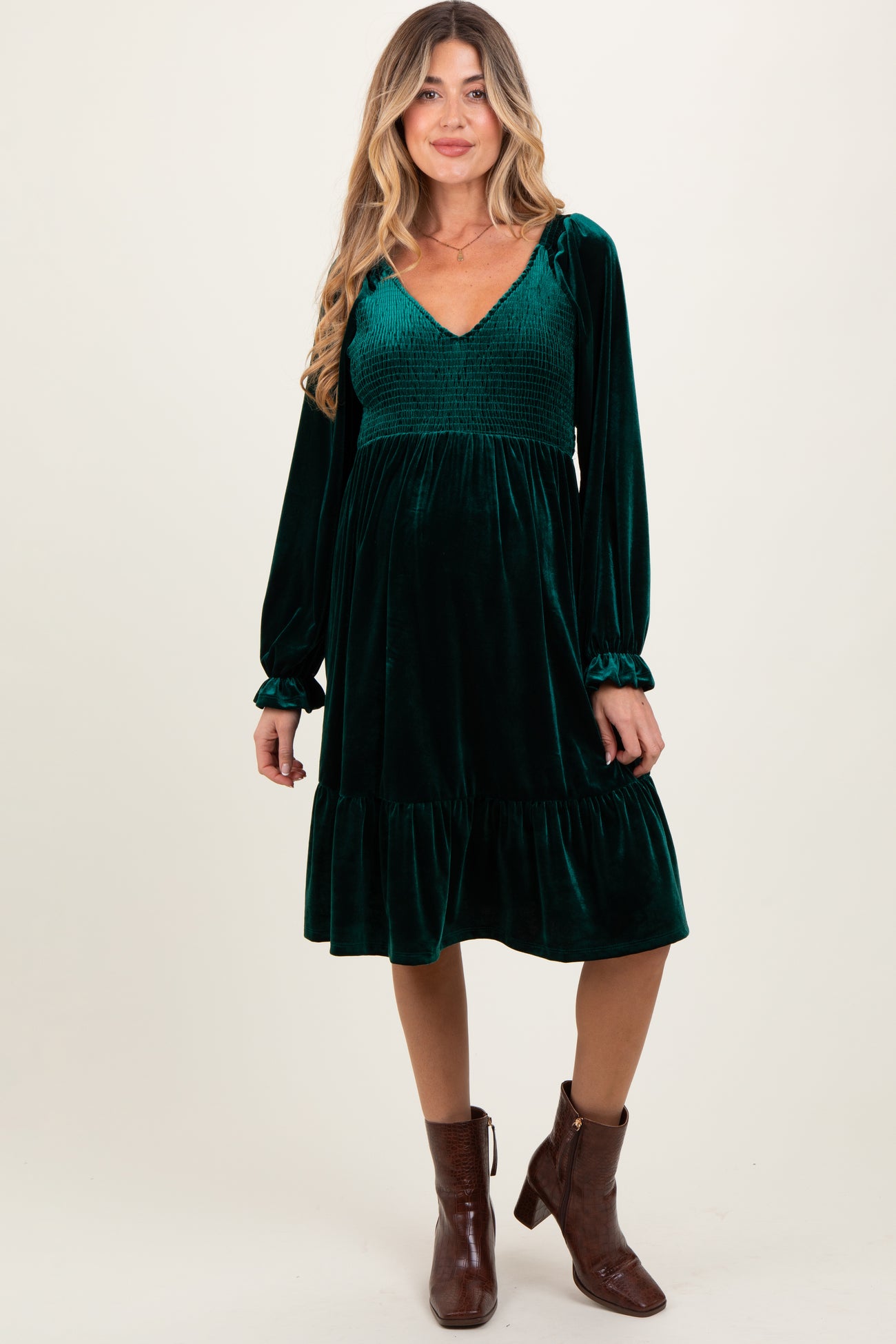woman wearing a green velvet maternity dress with a v-neck and tiered skirt, featuring long sleeves and a smocked bodice