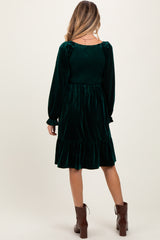 woman wearing a dark green velvet maternity dress with long sleeves and a ruffled hem