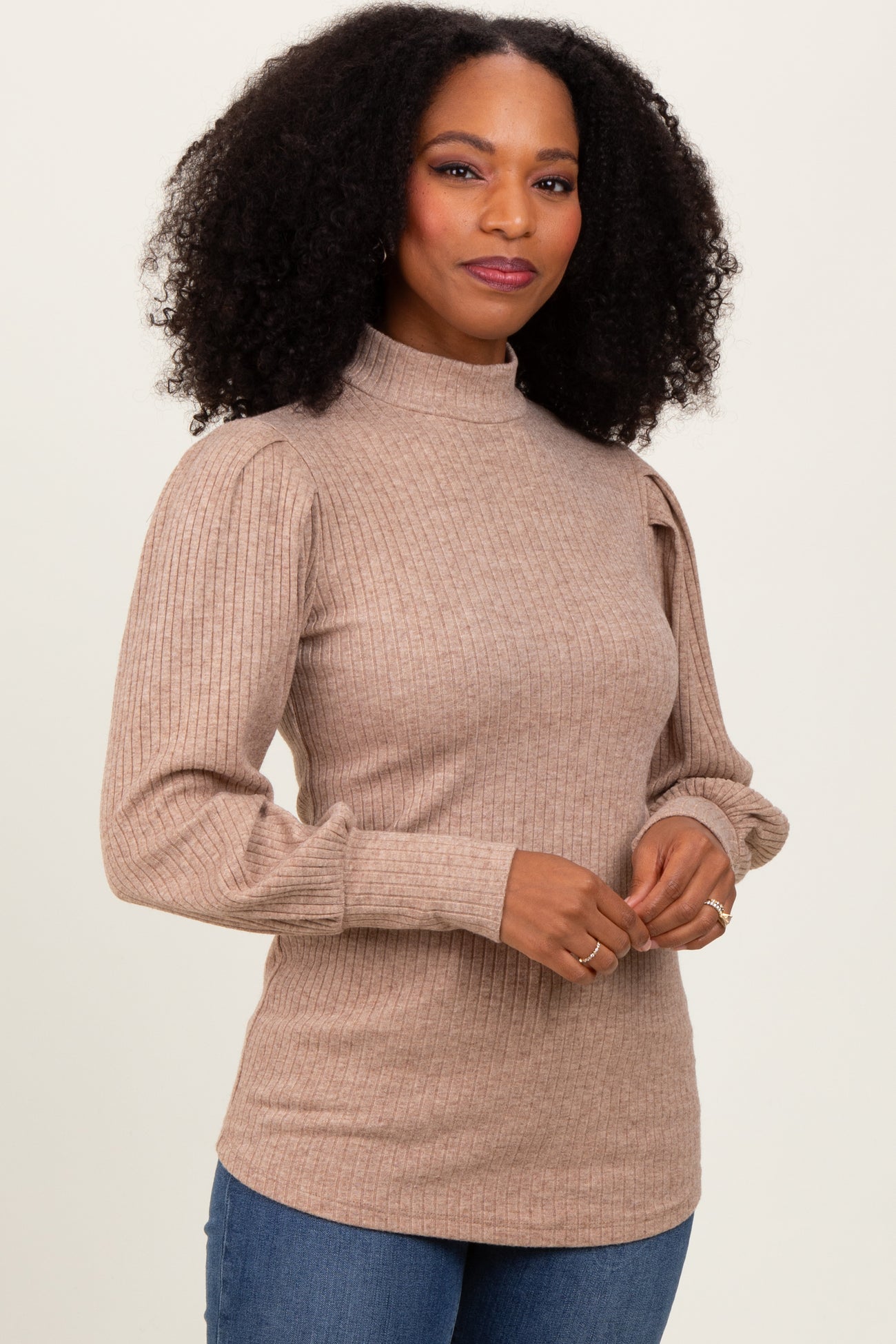woman wearing a tan ribbed mock neck sweater with puff sleeves and long sleeves, smiling at the camera