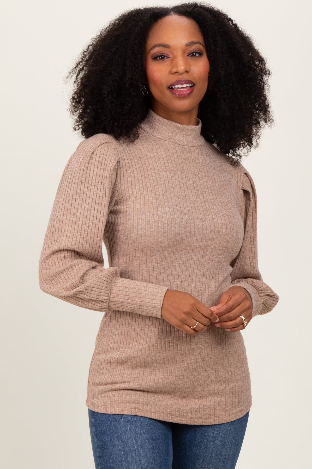 woman wearing a beige ribbed long sleeve top with puffed sleeves and a high neck, styled with blue jeans