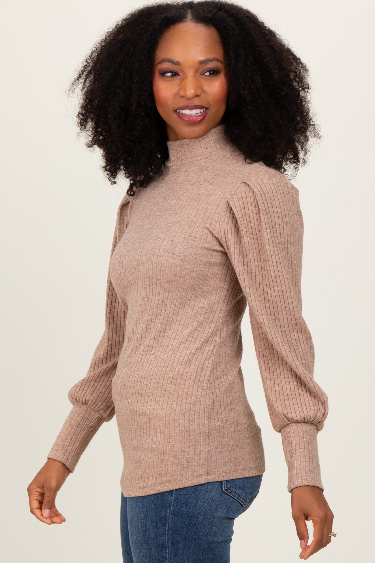 woman wearing a beige ribbed knit sweater with puffed long sleeves and a mock neck, paired with blue jeans