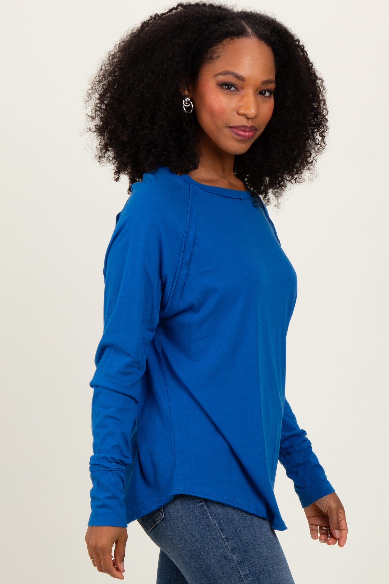 woman wearing a blue long sleeve relaxed fit top with side slits and a round neckline, styled with blue jeans