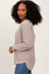 woman wearing a beige knit sweater with a relaxed fit and side slits, paired with blue jeans