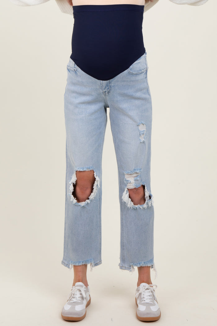 woman wearing light blue distressed maternity jeans with a navy blue over-the-bump band and white sneakers