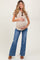woman wearing a beige maternity t-shirt and blue flared jeans, cradling her baby bump with a smile