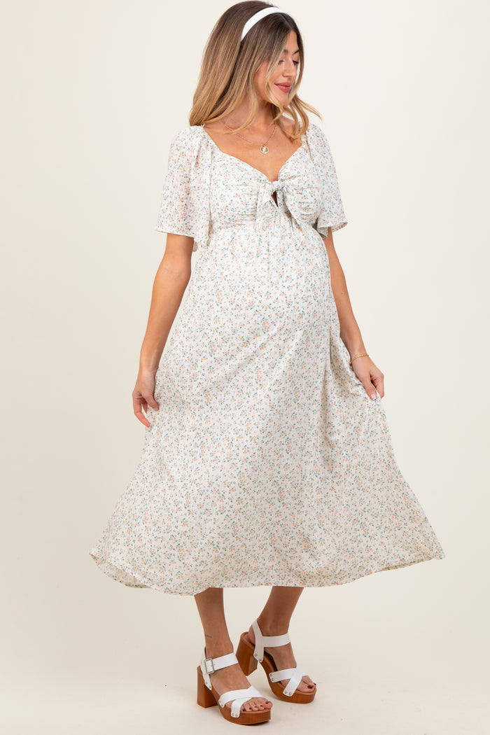 woman wearing a white floral maternity dress with short sleeves and a tie front, showing her baby bump