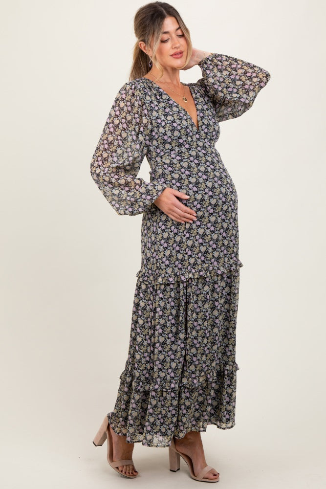 woman wearing a black floral maternity maxi dress with long sleeves and a ruffled hem, gently cradling her baby bump