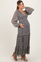woman wearing a black floral maternity maxi dress with long sleeves and a ruffled hem, gently cradling her baby bump