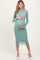 woman wearing a mint green long sleeve maternity dress, cradling her baby bump with both hands