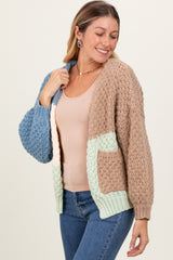 woman wearing a chunky knit cardigan in tan, blue, and mint with a pocket, paired with a nude tank top and jeans