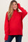 woman wearing a red turtleneck maternity sweater and blue jeans, smiling and touching her hair