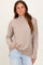 woman wearing a beige high neck sweater with side slits and long sleeves, styled with light blue jeans