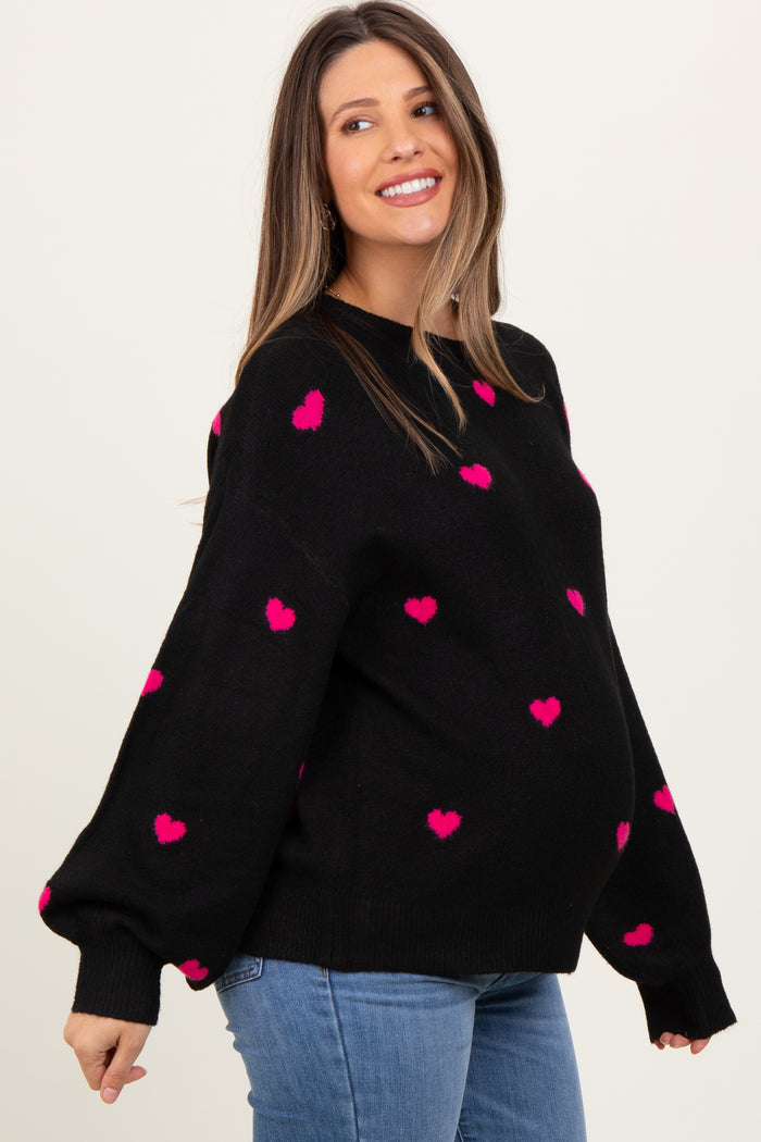 woman wearing a black maternity sweater with pink heart patterns and a visible baby bump