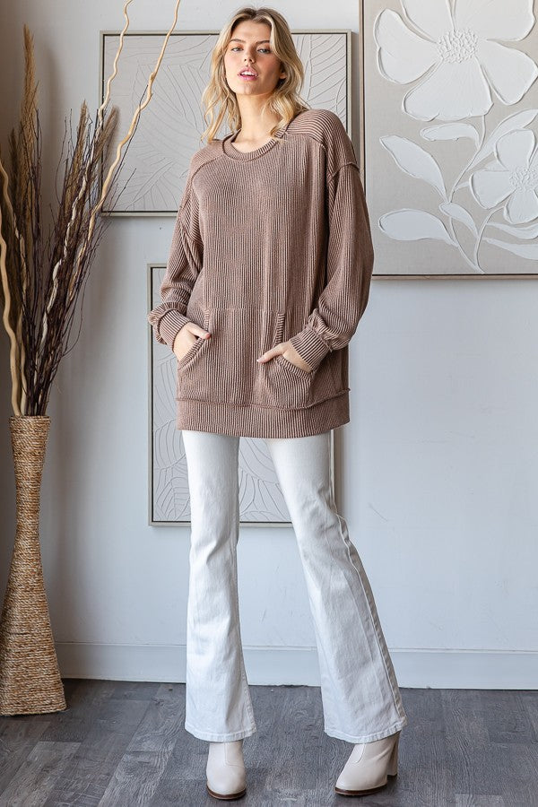 woman wearing a taupe oversized ribbed sweater with pockets and white flared jeans