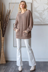 woman wearing a taupe oversized ribbed sweater with pockets and white flared jeans