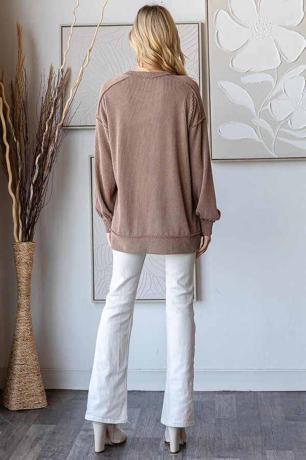 woman wearing a taupe ribbed oversized sweater and white flared jeans, standing with her back to the camera