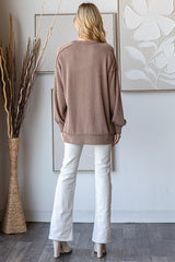 woman wearing a taupe ribbed oversized sweater and white flared jeans, standing with her back to the camera