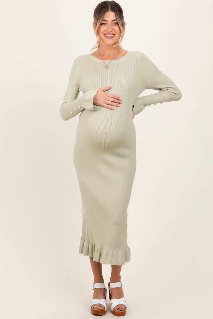 woman wearing a light green ribbed maternity dress with a ruffled hem and buttons on the sleeves, showing her baby bump