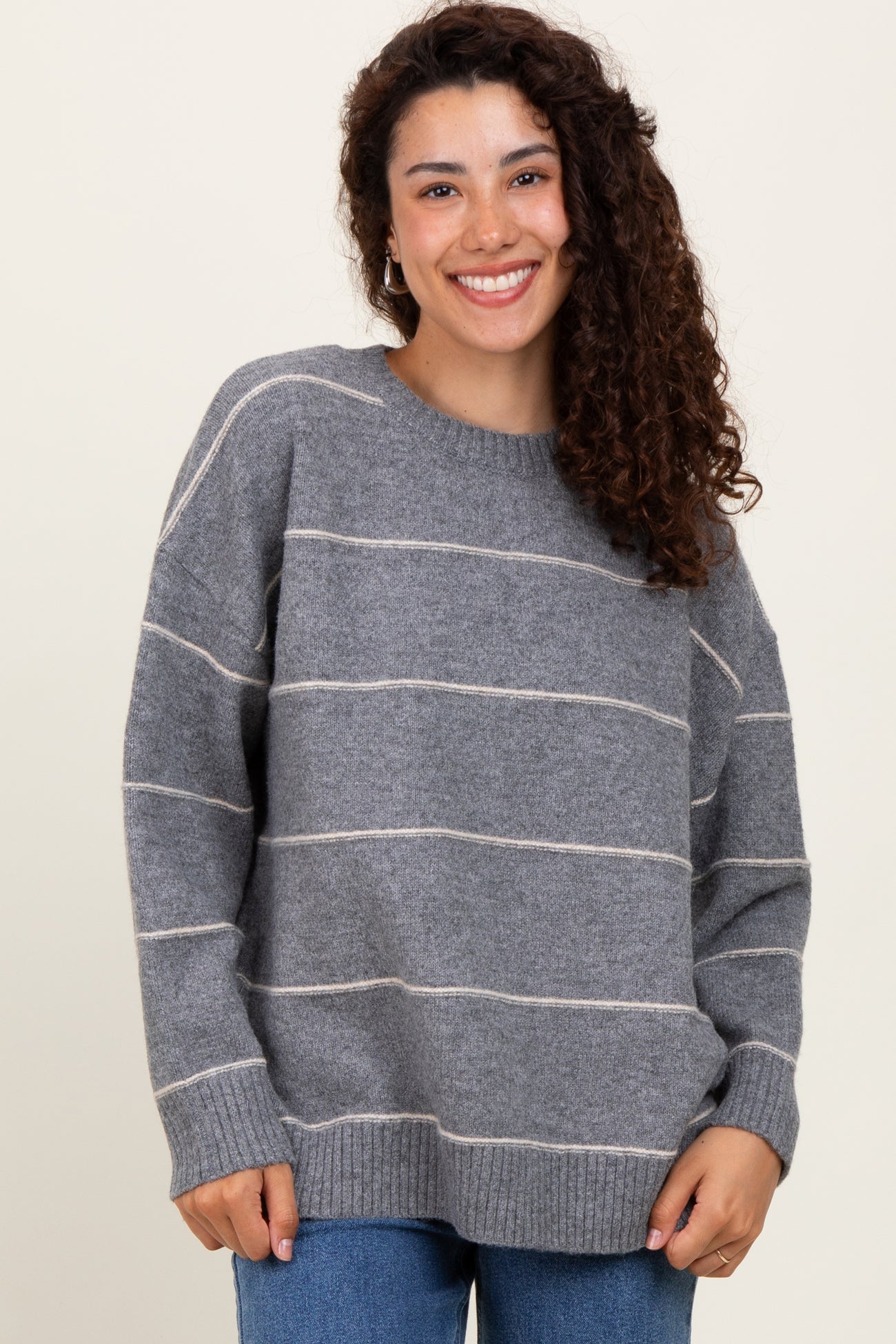 woman wearing a gray striped oversized sweater with a round neckline and smiling