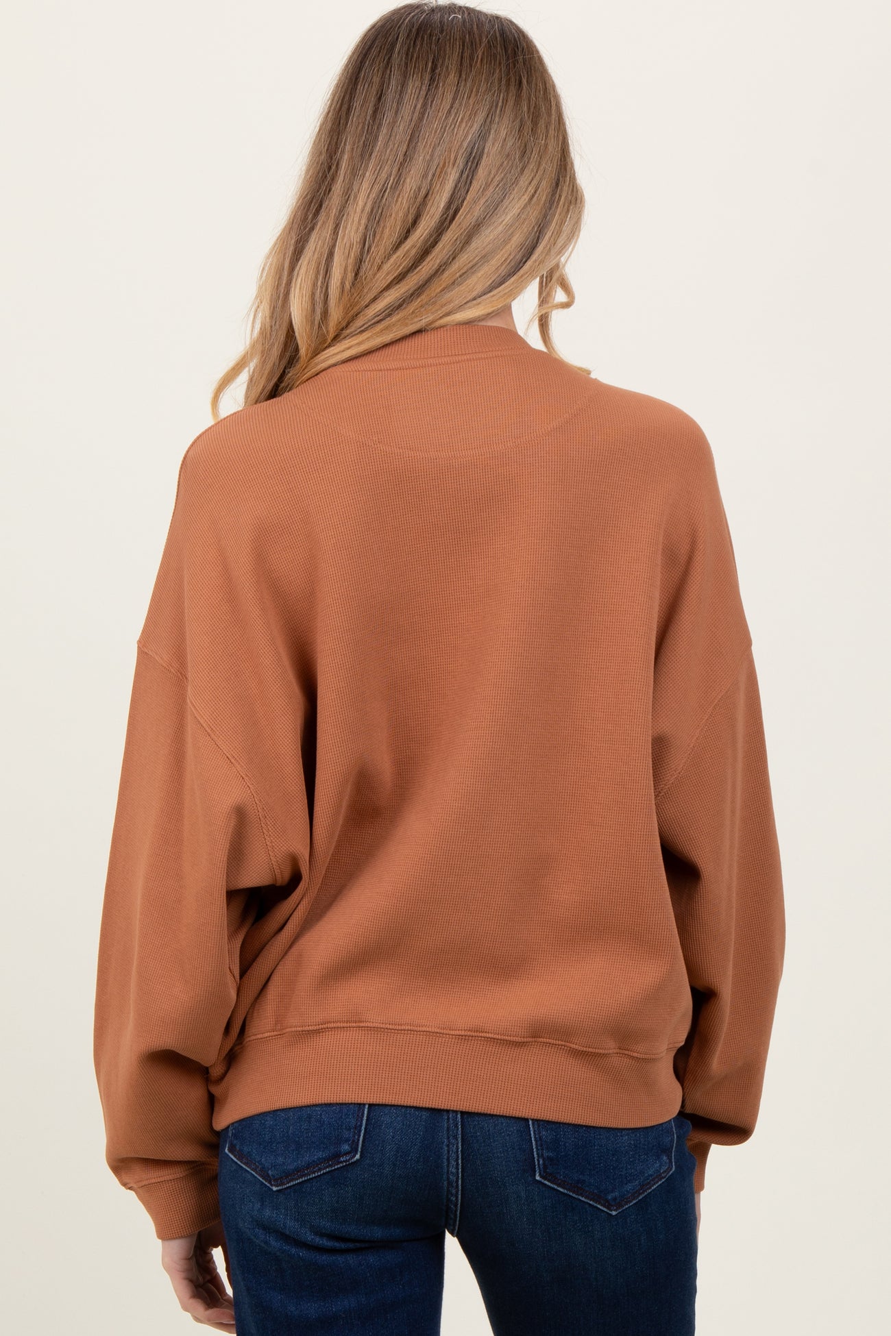 woman wearing a rust colored oversized maternity sweatshirt, viewed from the back
