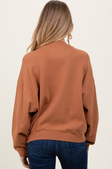woman wearing a rust colored oversized maternity sweatshirt, viewed from the back