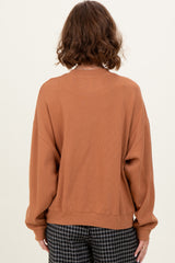 woman wearing a rust colored oversized sweater with long sleeves and a relaxed fit, viewed from the back