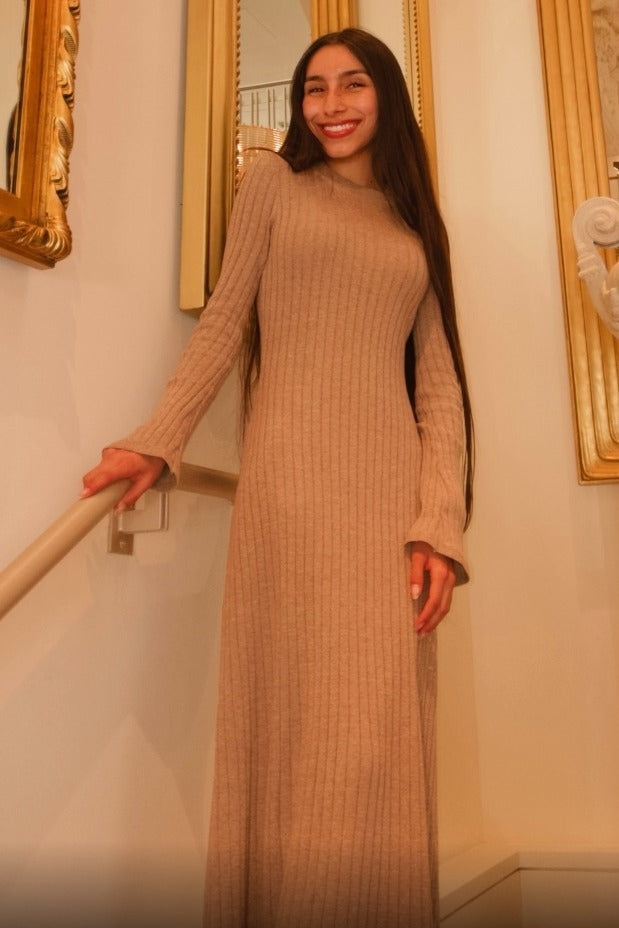woman wearing a long sleeve ribbed beige maxi dress with fitted silhouette, standing on staircase