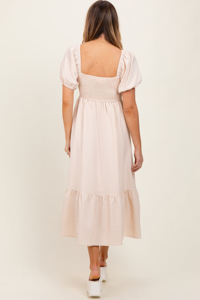 woman wearing a light pink striped maxi dress with puff sleeves and a smocked bodice, standing with her back to the camera