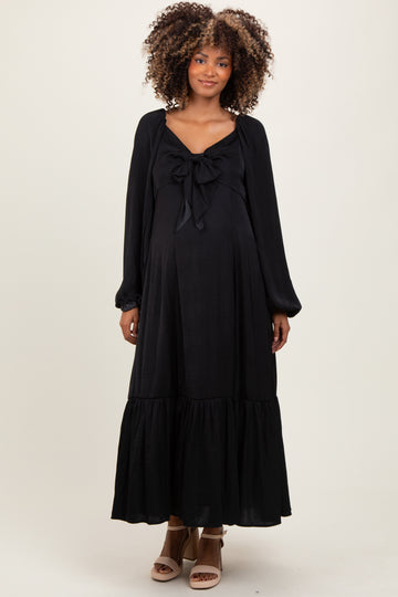 woman wearing a black maternity dress with a tie-front detail and long sleeves, showing a visible baby bump