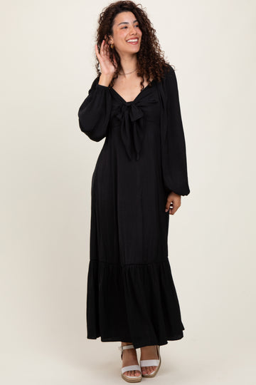 woman wearing a black maxi dress with a tie front and balloon sleeves, standing and smiling