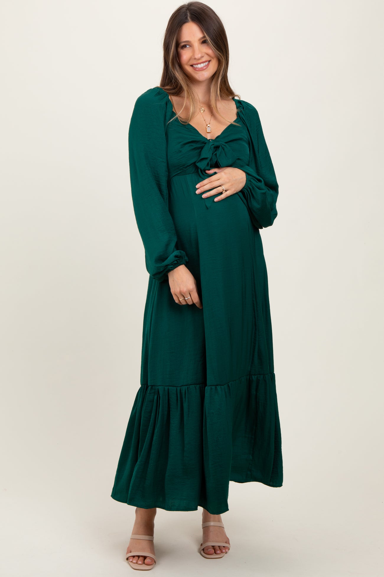 woman wearing a dark green maternity maxi dress with puff sleeves and a tie detail, holding her baby bump