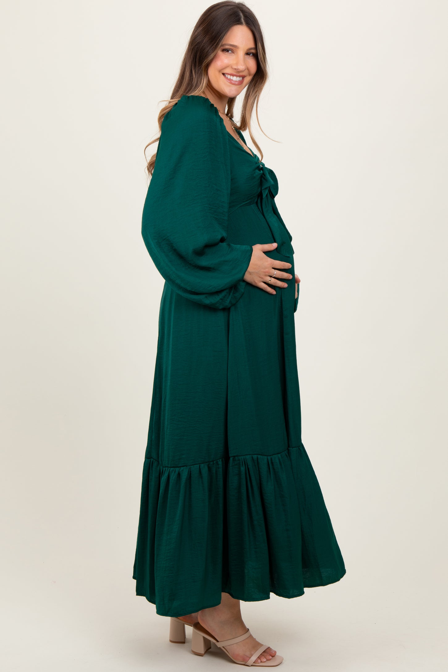 woman wearing a dark green maternity maxi dress with balloon sleeves and a ruffled hem, holding her baby bump
