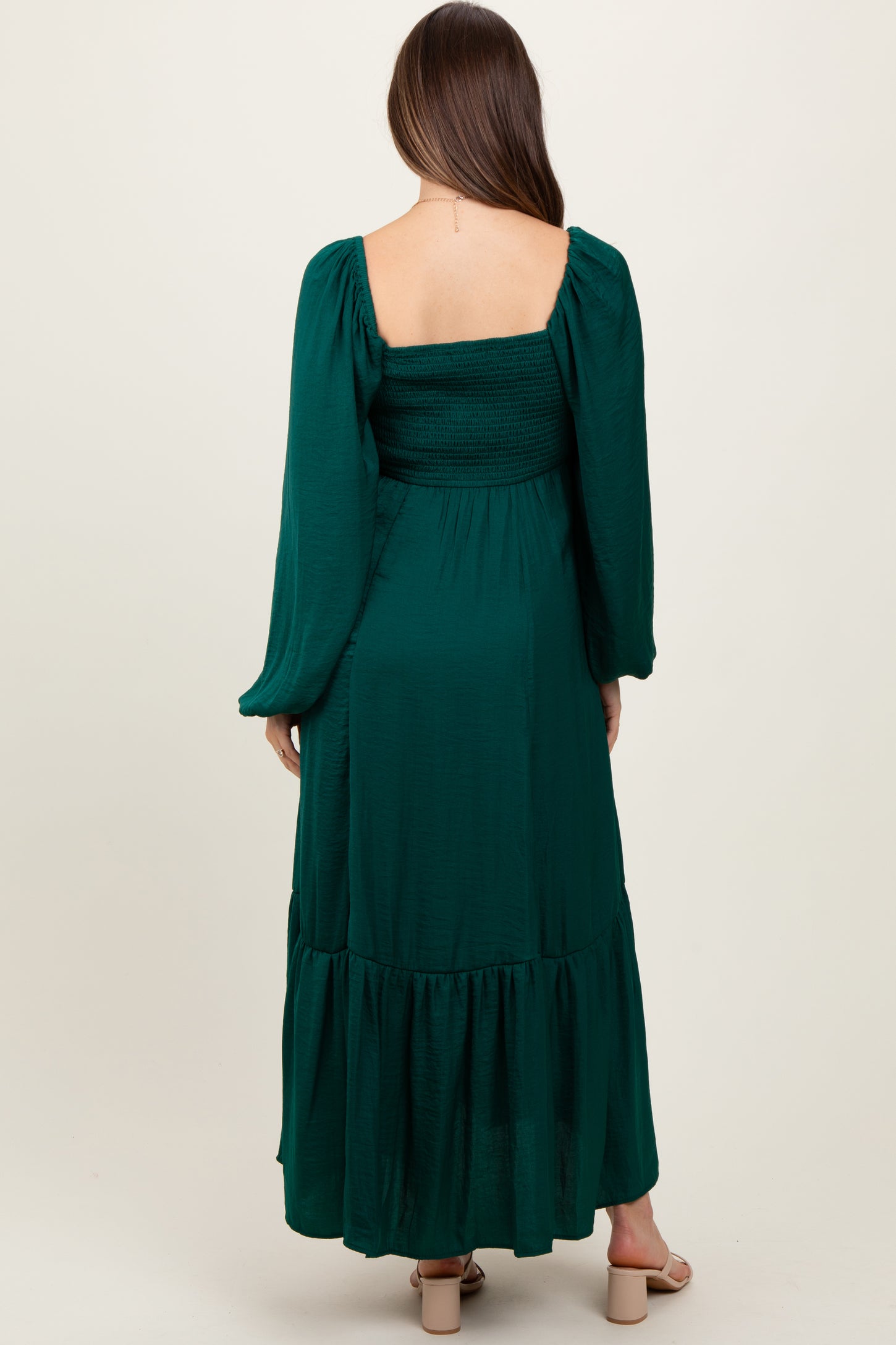 woman wearing a dark green long sleeve maternity dress with a smocked bodice and tiered skirt, showing no baby bump