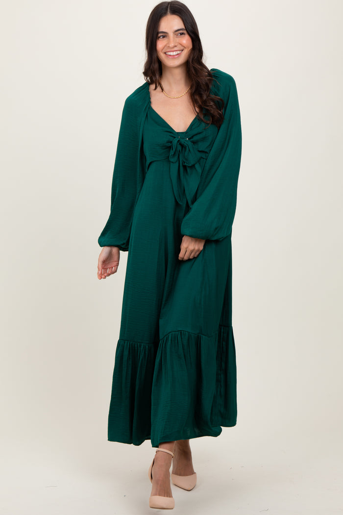woman wearing a green maxi dress with a knotted bodice and puff sleeves, standing with a smile on a neutral background
