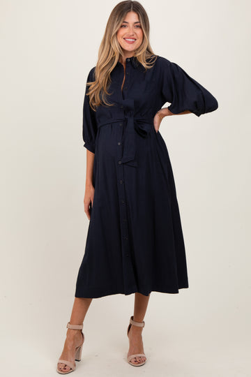 woman wearing a navy blue maternity dress with a tied waist and three-quarter sleeves, showing her baby bump