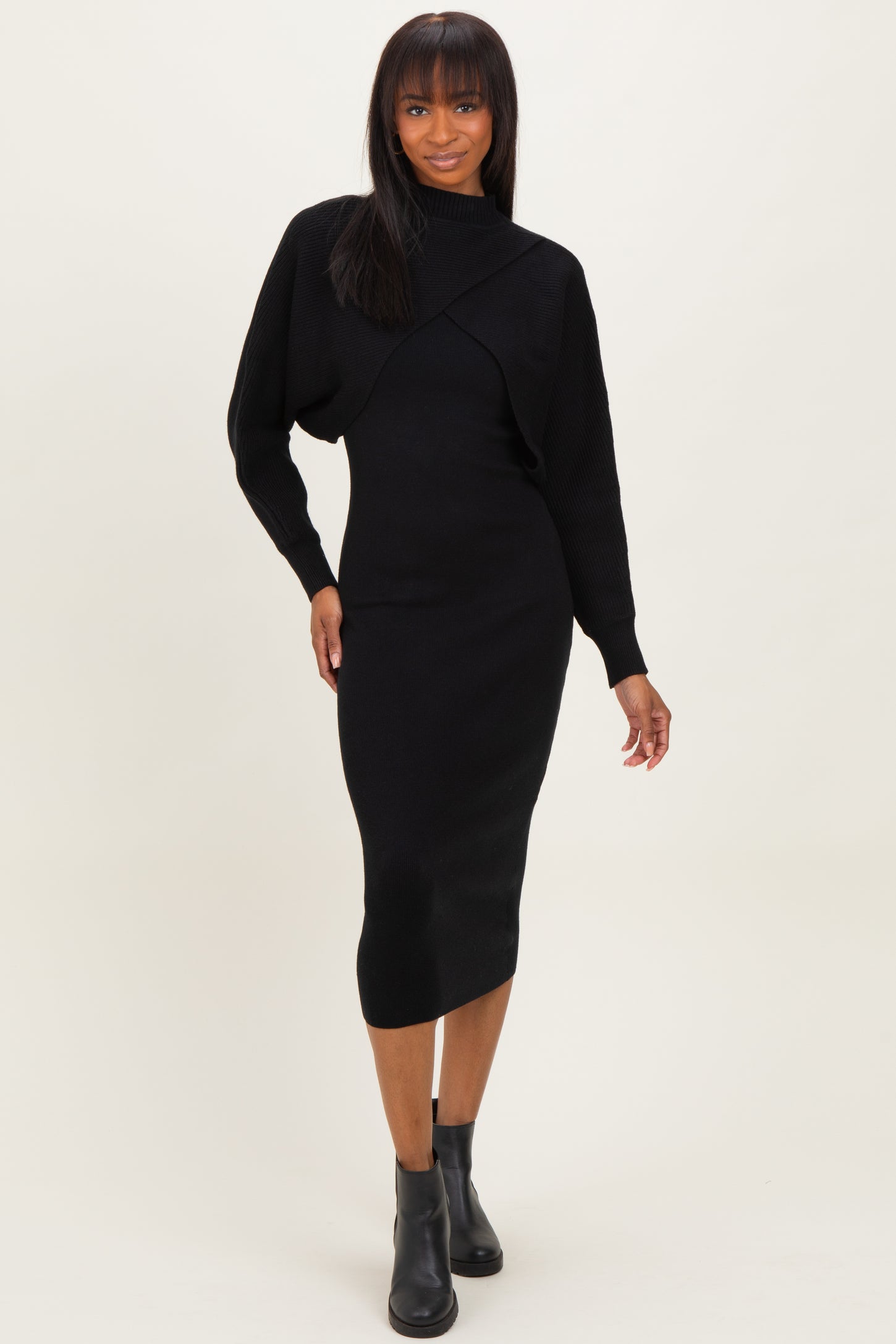 woman wearing a black long sleeve fitted midi dress with a textured overlay and ankle boots