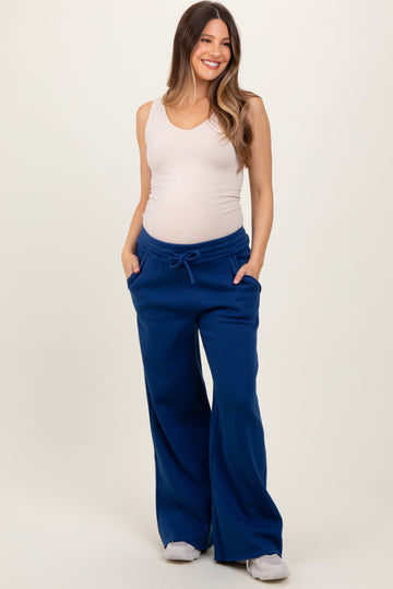 woman wearing a light brown sleeveless top and navy maternity jogger pants with pockets, showing a baby bump
