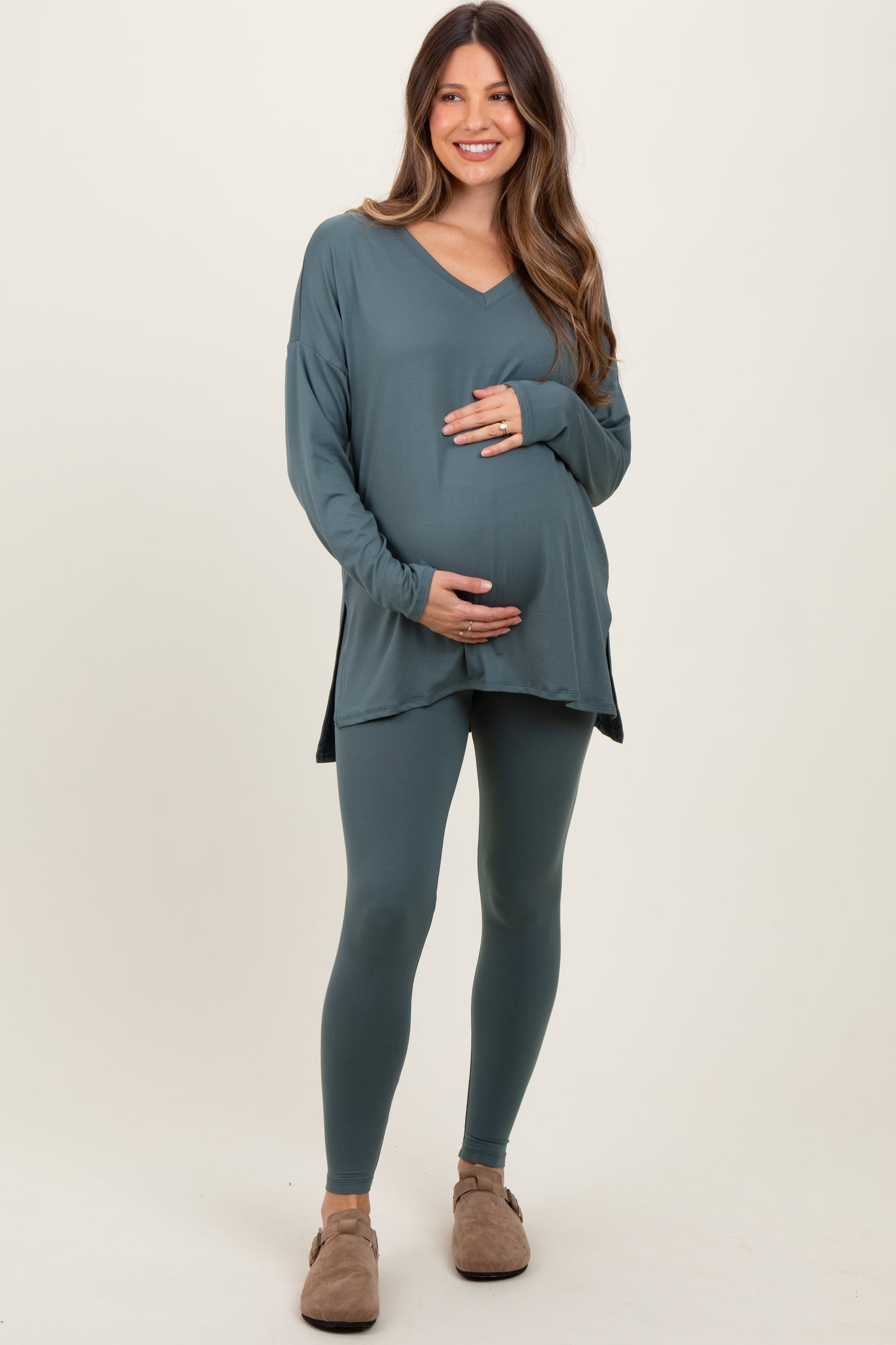 woman wearing a teal long sleeve maternity top and matching leggings, holding her baby bump