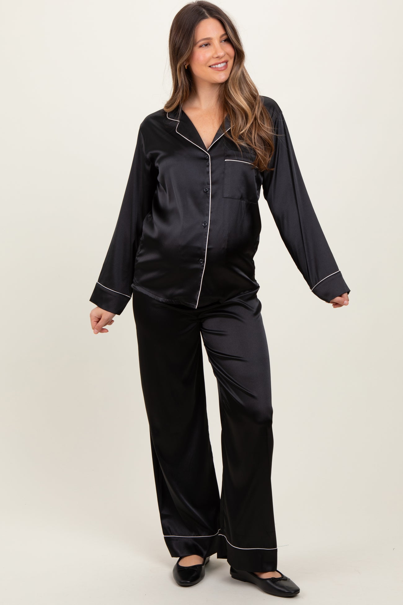 woman wearing a black satin maternity pajama set with piping details and a visible baby bump