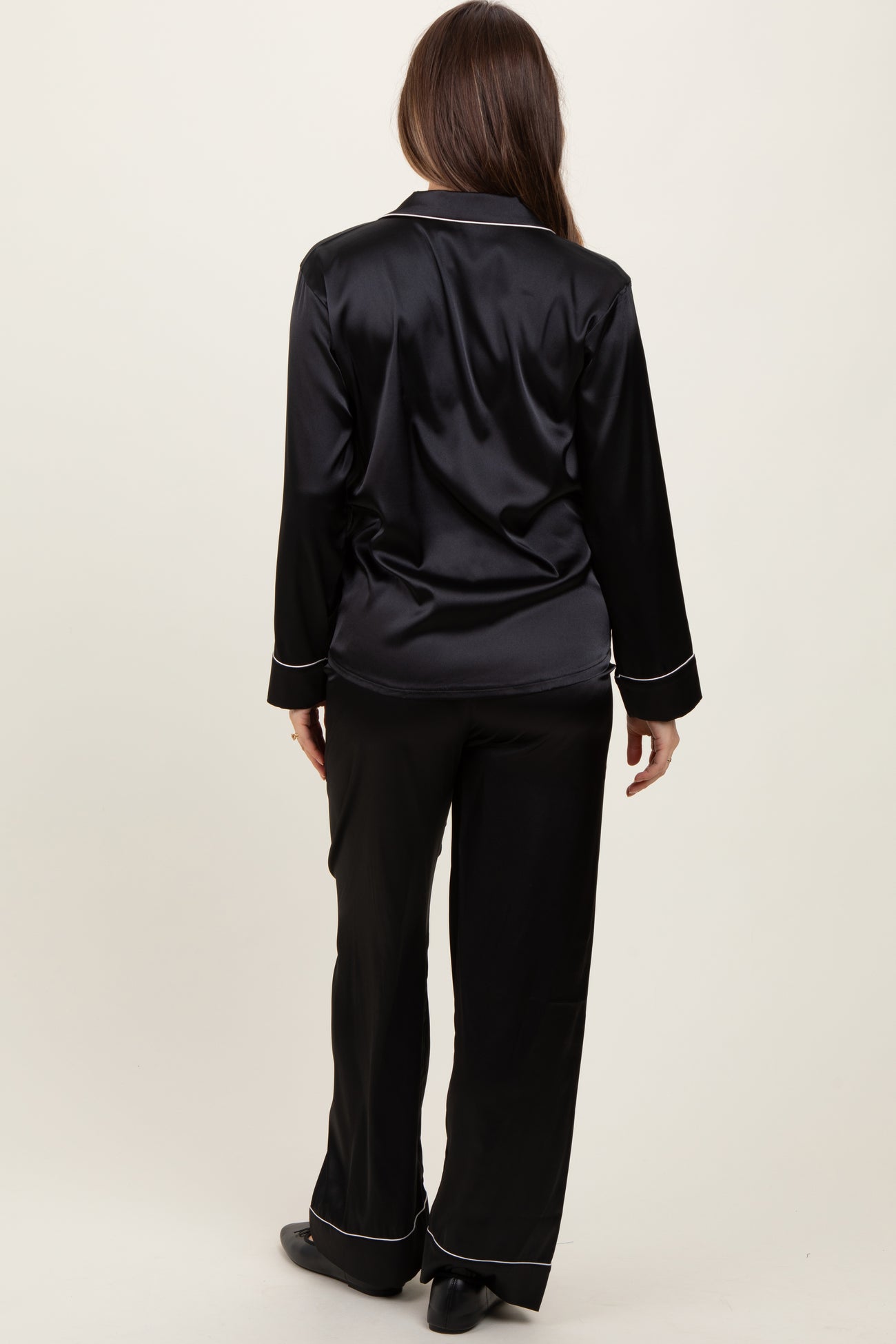 woman wearing a black satin maternity pajama set with long sleeves and matching pants, seen from the back