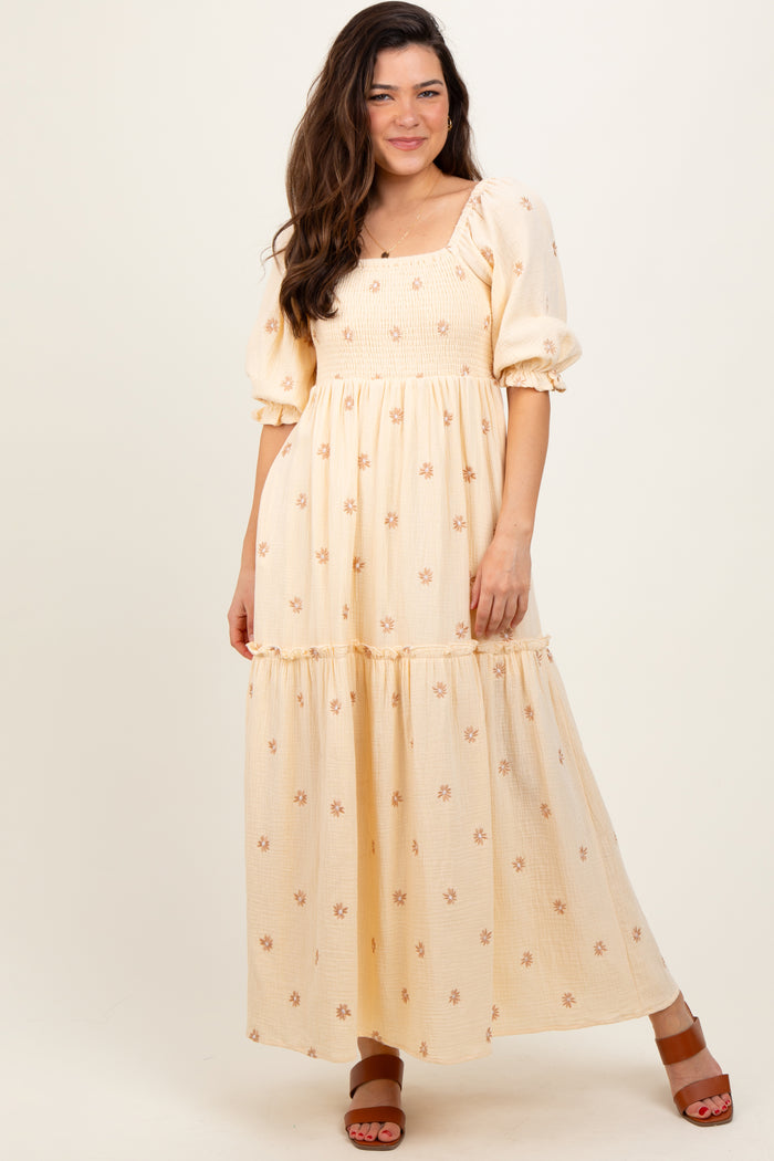 woman wearing a yellow puff sleeve maxi dress with floral details and a tiered skirt, standing against a neutral background