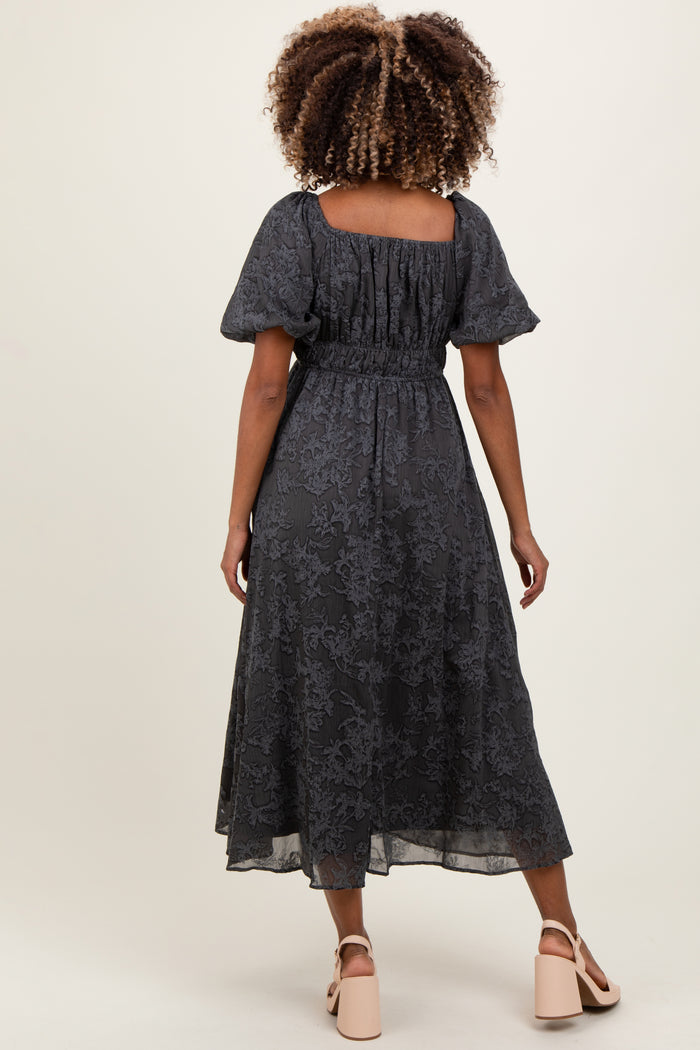 woman wearing a dark gray floral maternity dress with puff sleeves and a smocked waist, showing a baby bump