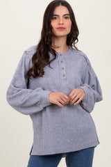 woman wearing a gray oversized long sleeve button-up sweater with pleated shoulders and side slits