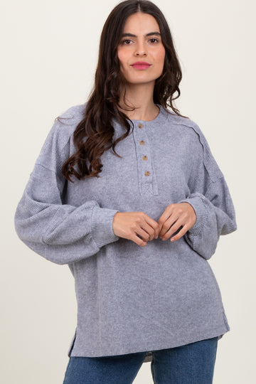 woman wearing a gray oversized long sleeve button-up sweater with pleated shoulders and side slits
