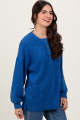 woman wearing a blue oversized button-up sweater with long sleeves and side slits, smiling while standing against a neutral background